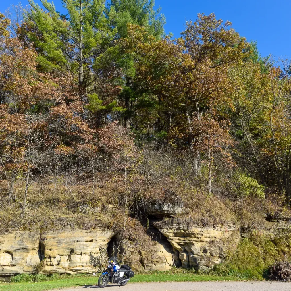 A sandstone formation behind a Triumph motorcycle in Wisconsin with trees sporting fall colors.