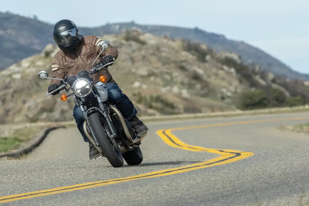 2026 Triumph Bonneville T100 being ridden on a twisty road in the mountains.