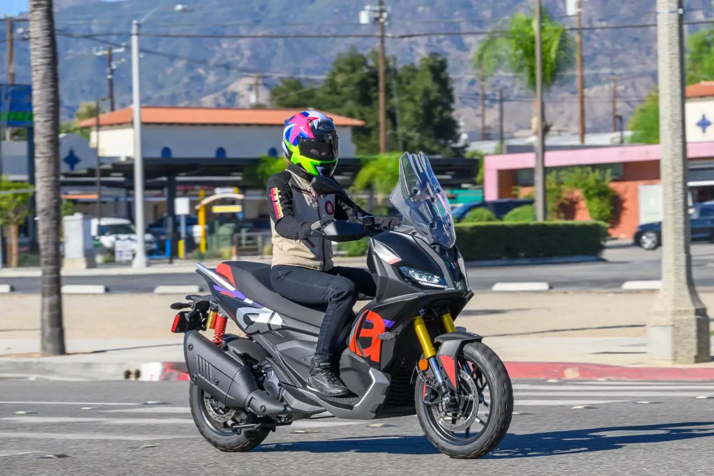 Riding the 2027 Aprilia SR GT 400 through town with a parking lot and utility pols in the background.
