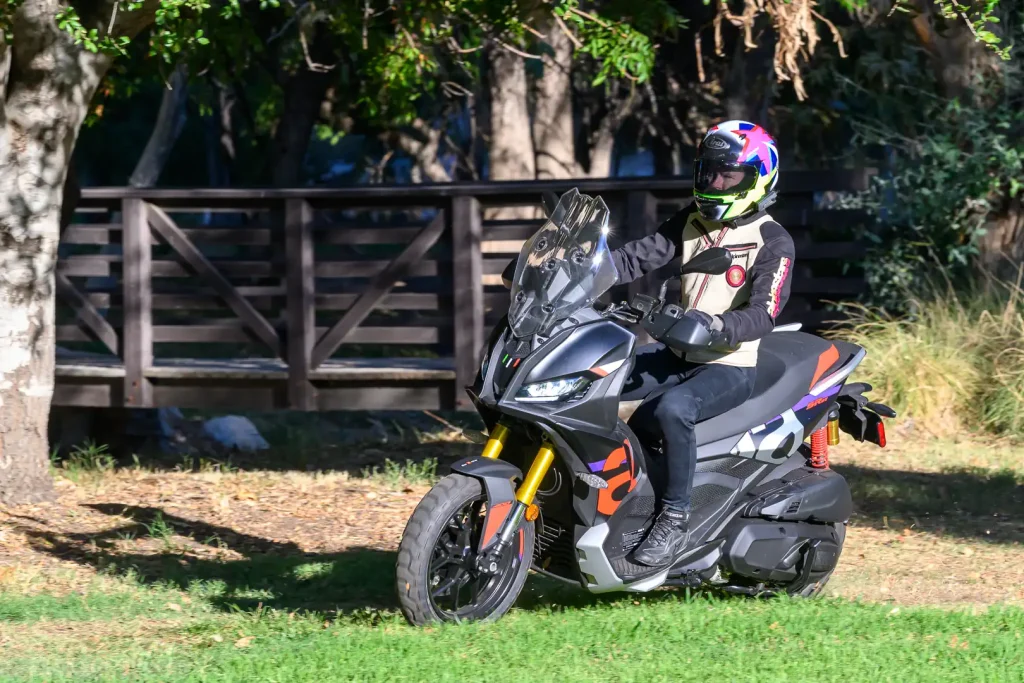 The 2027 Aprilia SR GT 400 is being ridden off-road with a bridge in the background.