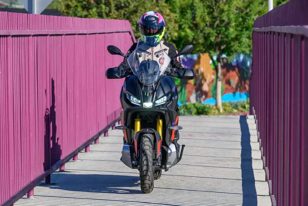 Riding over a narrow bridge with purple safety barrier on the 2027 Aprilia SR GT 400 .