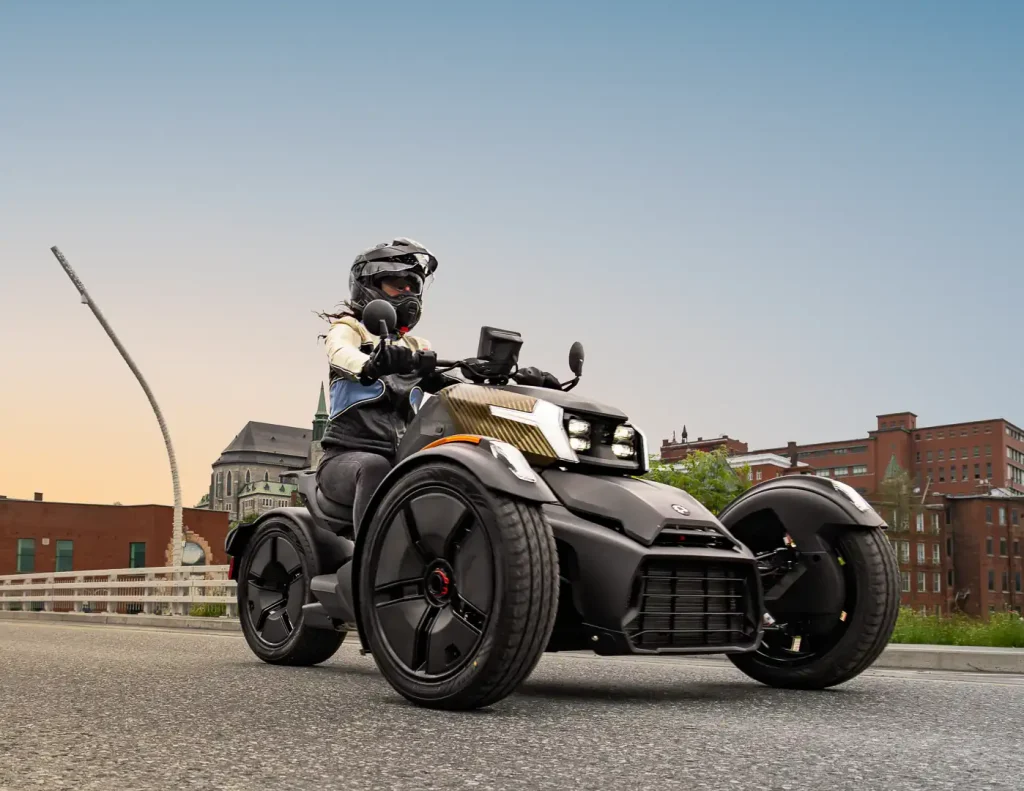 2027 Can-Am Ryker being ridden down the street at golden hour with brick buildings in teh background.