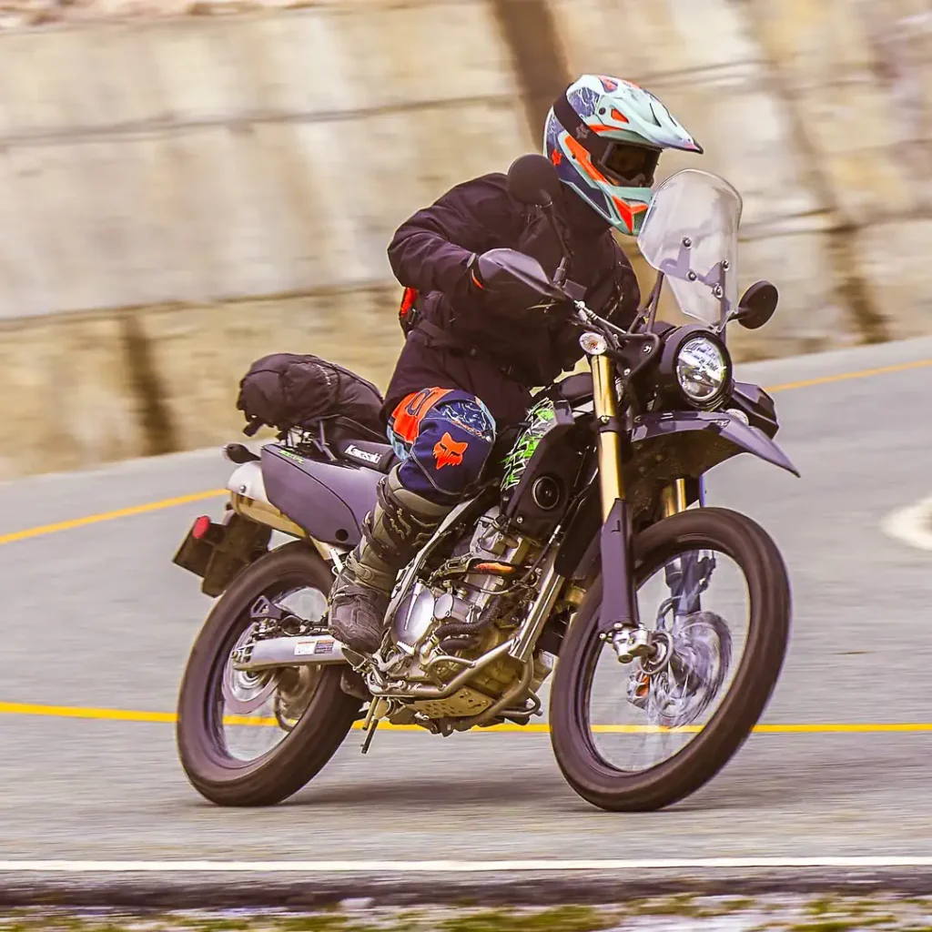 The 2027 Kawasaki KLX300 XPL leaned to the left going around a corner on pavement.