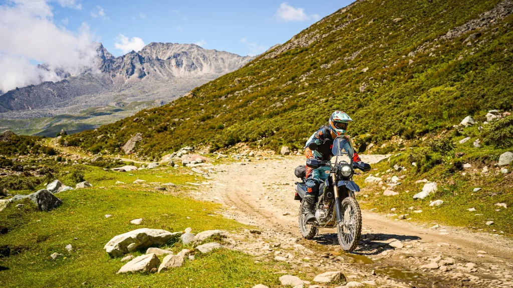 The 2027 Kawasaki KLX300 XPL riding down a dirt road with a mountain in the background