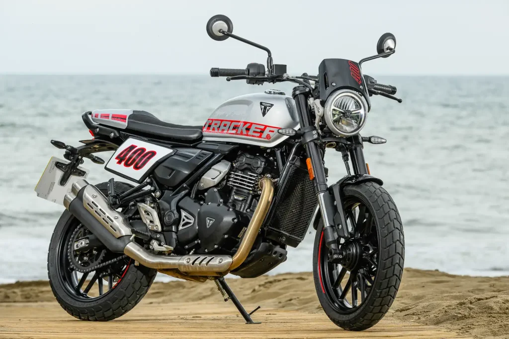A front 3/4 right side view of the 2027 Triumph Tracker 400 in front of the Mediterranean Sea.