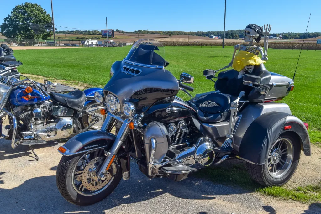 A skeleton sits on the passenger seat of a Harley-Davidson Tri Glide.