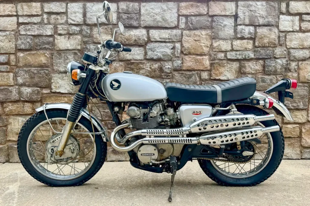 Scrambler Motorcycle History: 1968 Honda CL450 parked with a rock wall behind it.