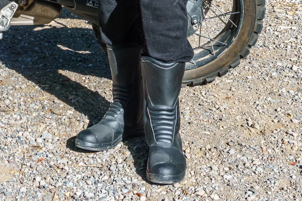 A stylish foot pose showing of the Xpd X-Venture H2Out boots with a motorcycle behind them.