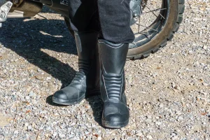 A stylish foot pose showing of the Xpd X-Venture H2Out boots with a motorcycle behind them.